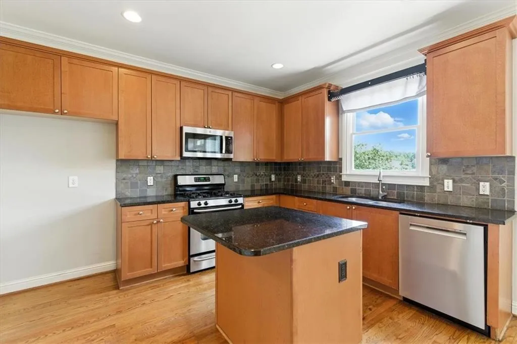 Kitchen featuring appliances with stainless steel finishes, ornamental molding, a kitchen island, light wood finished floors, and dark stone counters