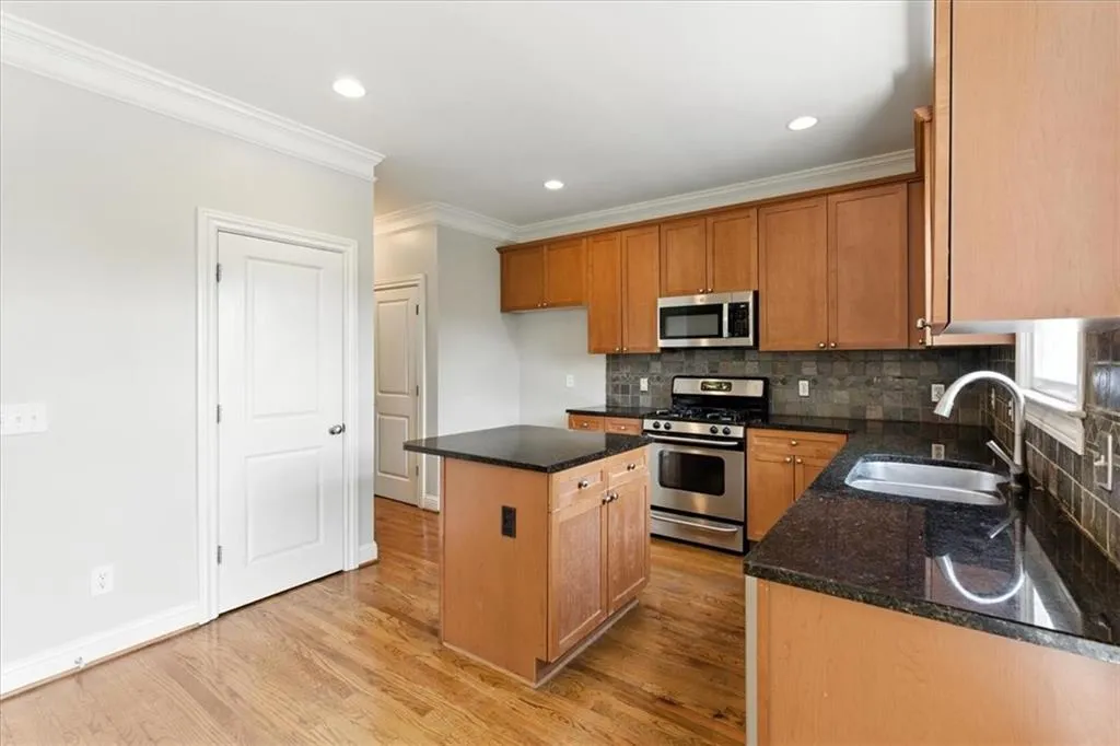 Kitchen featuring appliances with stainless steel finishes, decorative backsplash, a kitchen island, ornamental molding, and light wood finished floors