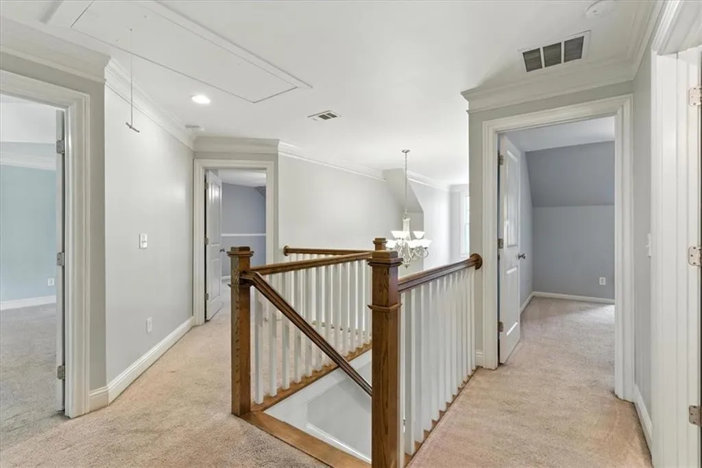Hall featuring attic access, light carpet, a chandelier, an upstairs landing, and crown molding
