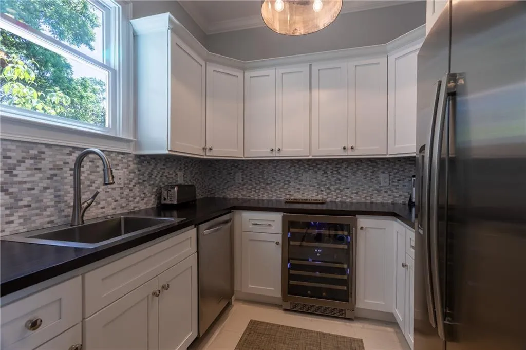 Kitchen featuring beverage cooler, tasteful backsplash, white cabinetry, appliances with stainless steel finishes, and sink
