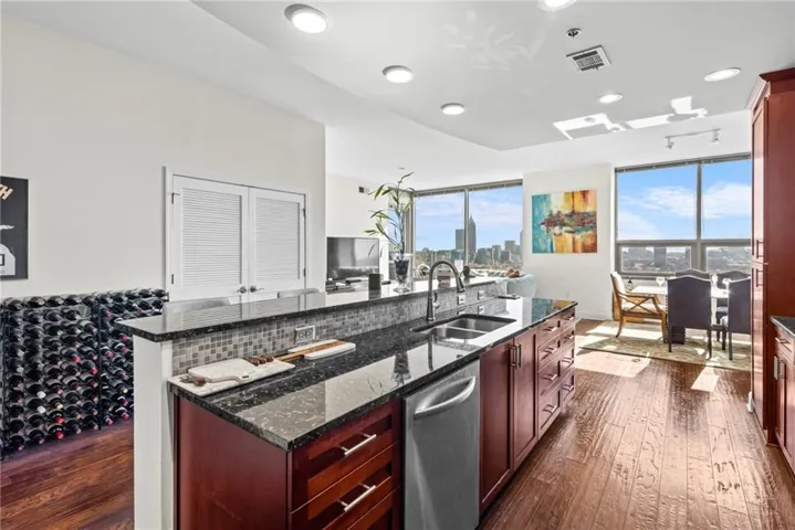 Kitchen featuring dark stone counters, reddish brown cabinets, a center island with sink, stainless steel dishwasher, and dark wood-type flooring