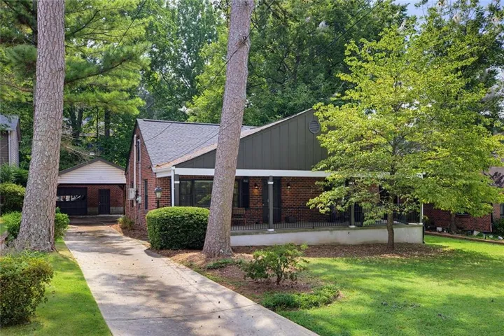 Brick exterior with a covered porch, an attached carport, a paved driveway, mature trees, and established landscaping