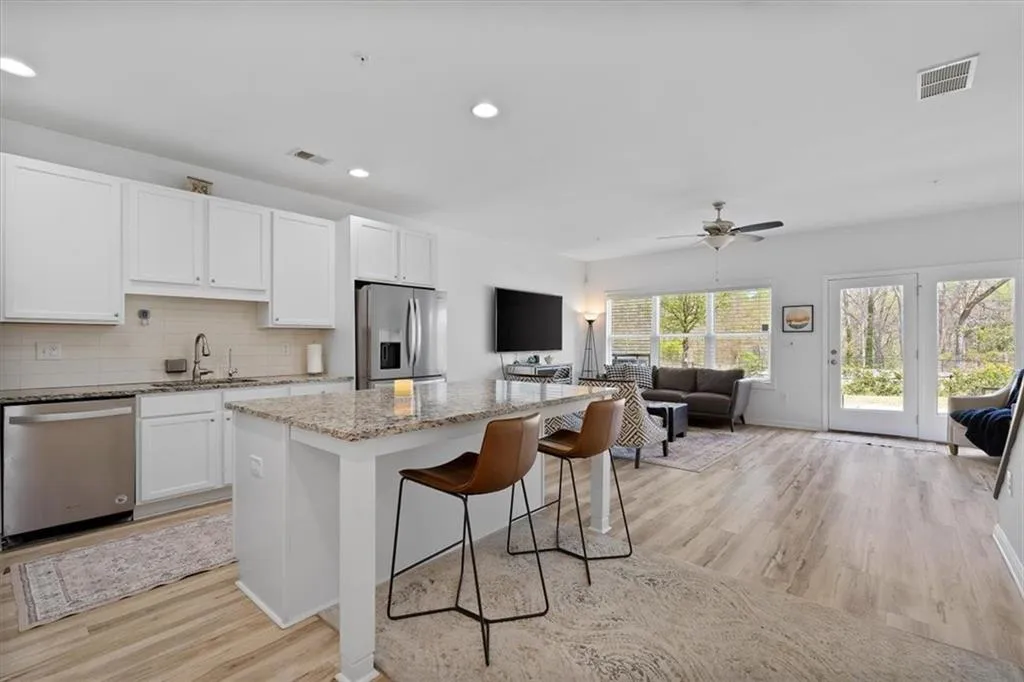 Kitchen with light stone counters, open floor plan, stainless steel appliances, white cabinets, and recessed lighting