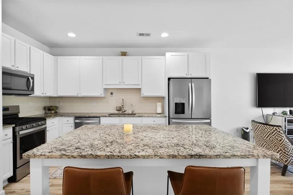 Kitchen with light wood finished floors, stainless steel appliances, a breakfast bar area, light stone counters, and a kitchen island
