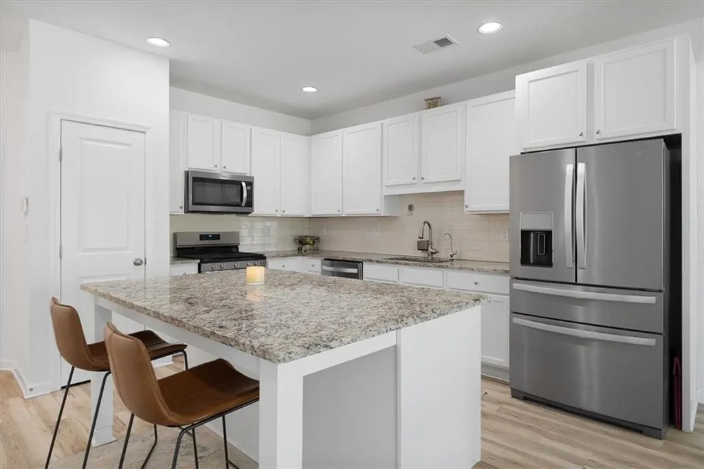 Kitchen featuring stainless steel appliances, light stone counters, light wood-style floors, a kitchen bar, and recessed lighting