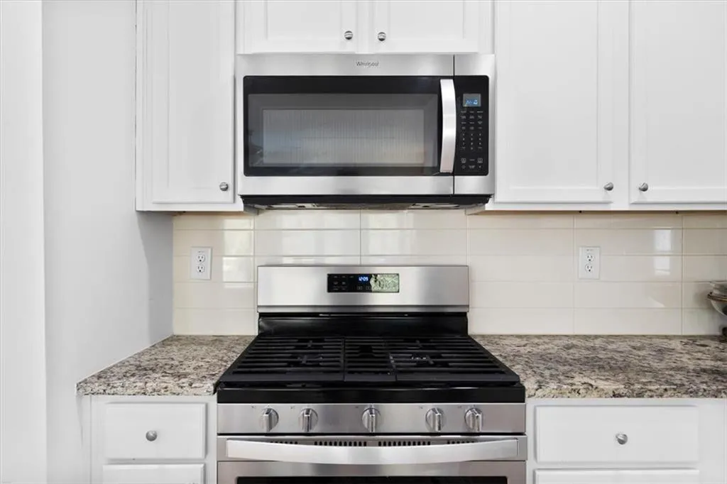 Kitchen featuring stainless steel appliances, white cabinets, light stone countertops, and decorative backsplash