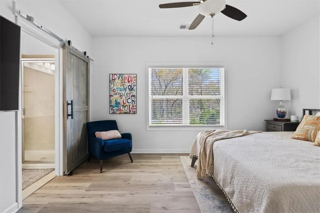 Bedroom featuring a barn door, light wood-style flooring, ceiling fan, and ensuite bath