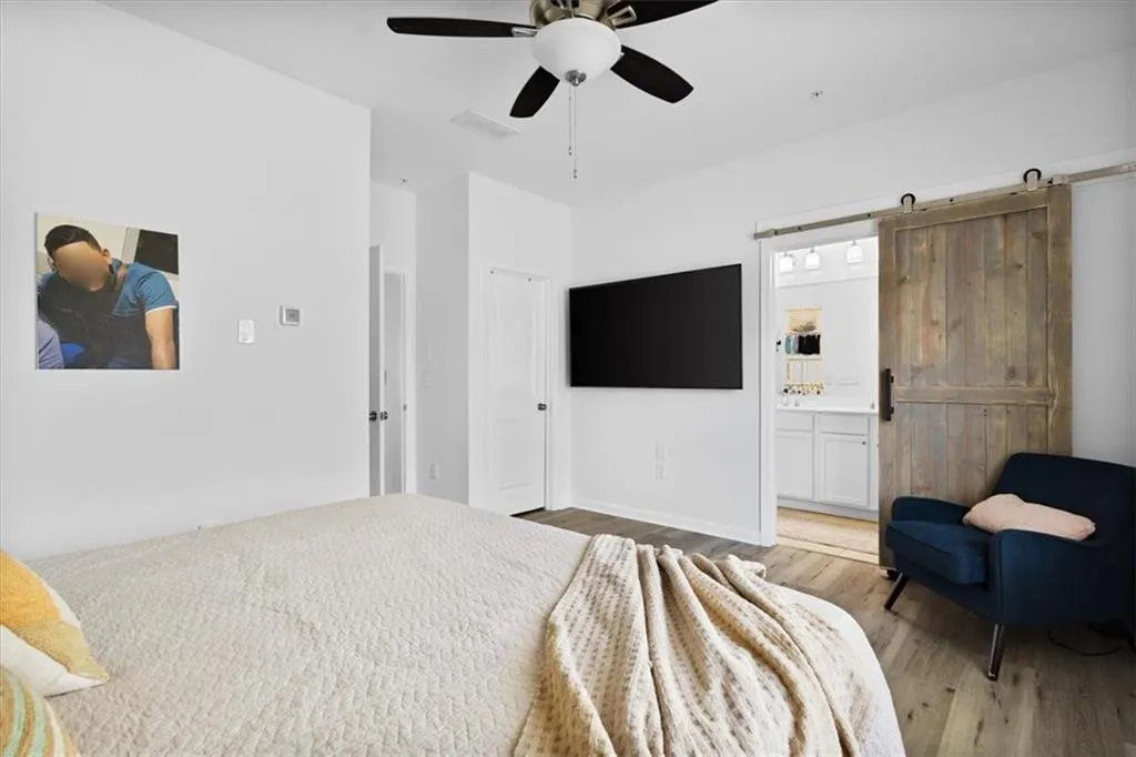 Bedroom with a barn door, light wood finished floors, a ceiling fan, and ensuite bathroom