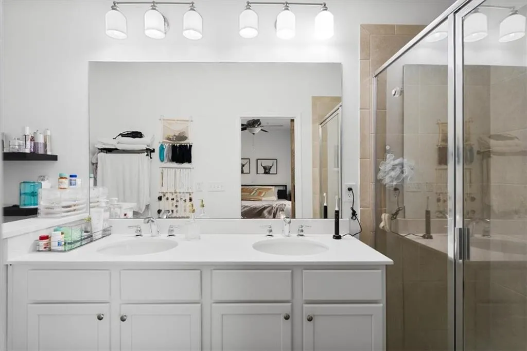 Ensuite bathroom featuring double vanity, a shower stall, and ceiling fan