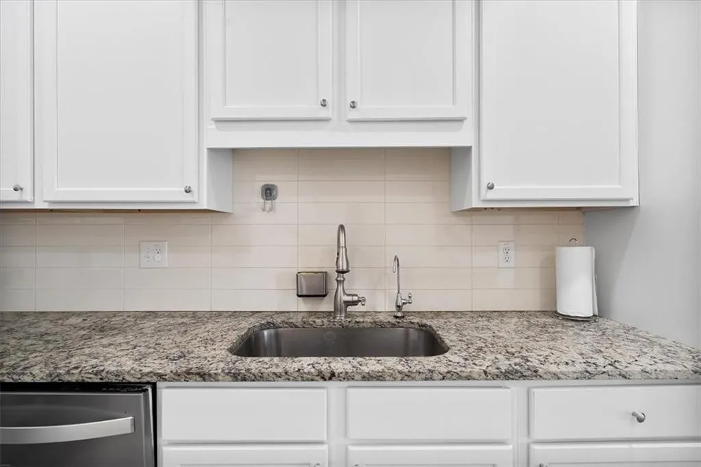 Kitchen featuring white cabinets, light stone countertops, stainless steel dishwasher, and tasteful backsplash