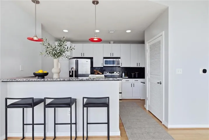 Kitchen featuring white cabinetry, stainless steel appliances, black tile backsplash, and a breakfast bar with a speckled countertop