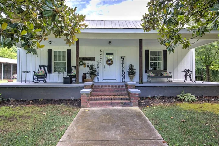 Classic farmhouse exterior with a welcoming front porch featuring white painted columns, brick steps, and a metal roof