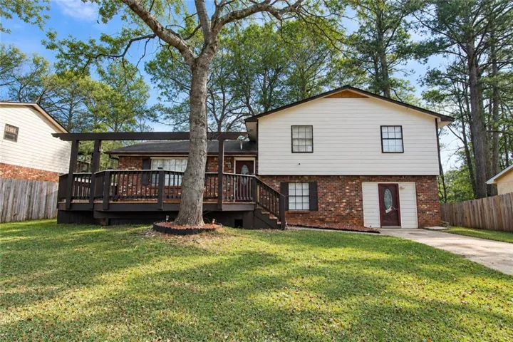 Exterior featuring brick and white siding, an expansive wooden deck, a paved driveway, and a front lawn with mature trees