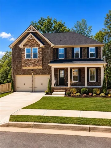 Traditional brick exterior featuring a covered porch with white columns, a two-car garage, and a manicured front lawn