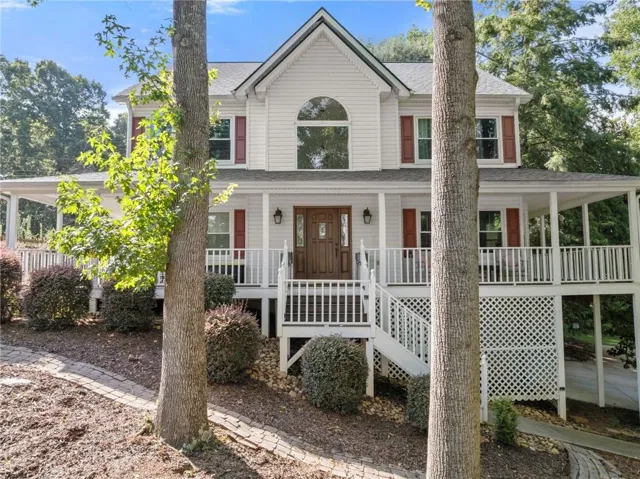 White siding exterior with a prominent arched window, a full-width covered porch with white railings, and a double wood-finish entry door with sidelights