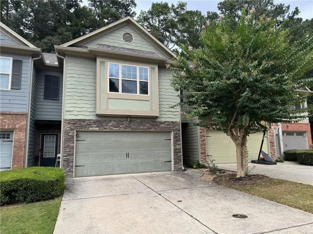 Front exterior with green siding, stone accents, and an attached two-car garage