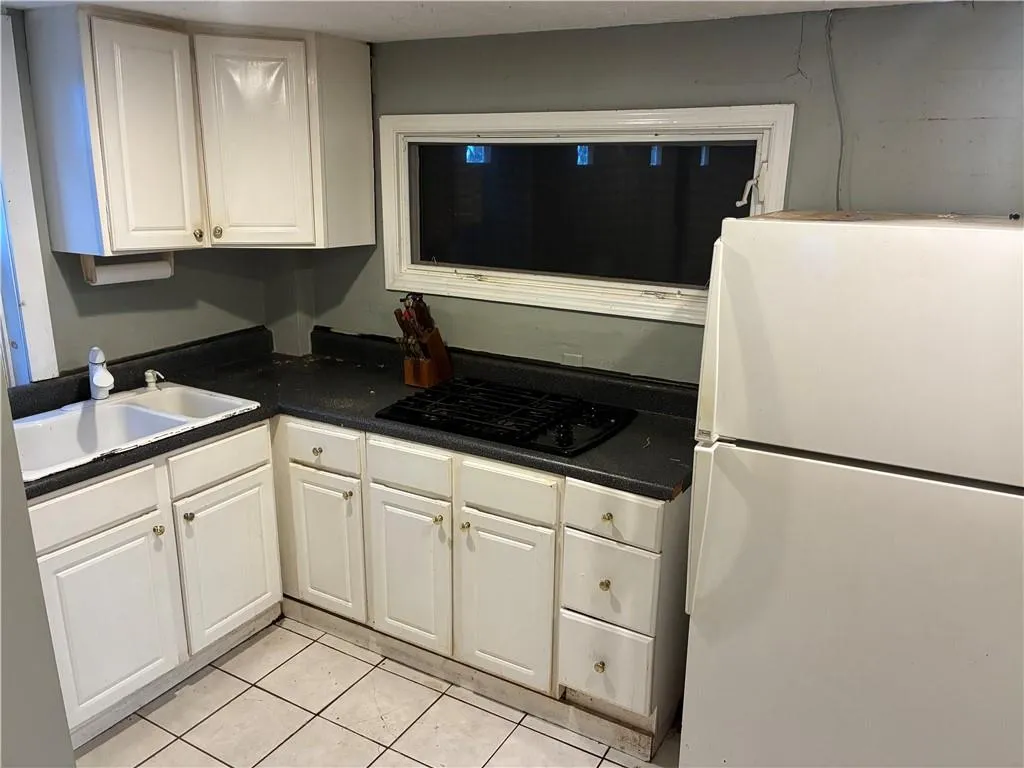 Kitchen with freestanding refrigerator, dark countertops, white cabinets, light tile patterned floors, and black gas stovetop