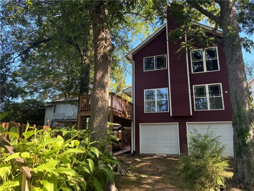 Mid-century inspired home with a wooden deck, an attached garage, a chimney, and dirt driveway