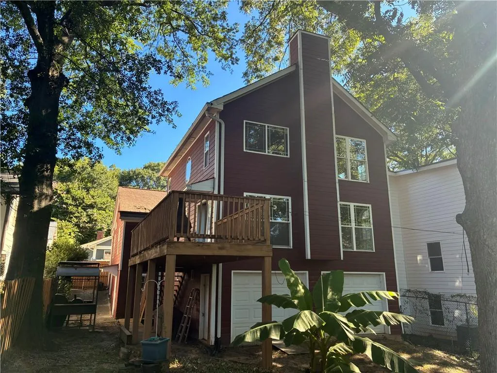 Back of property with a deck, an attached garage, and a chimney