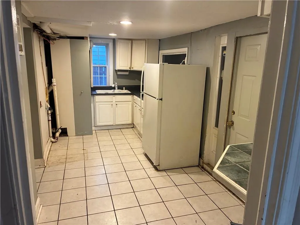 Kitchen with dark countertops, freestanding refrigerator, white cabinetry, and light tile patterned floors