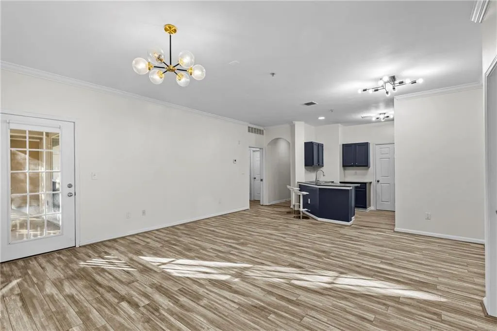 Unfurnished living room featuring arched walkways, crown molding, light wood finished floors, and suspended lighting