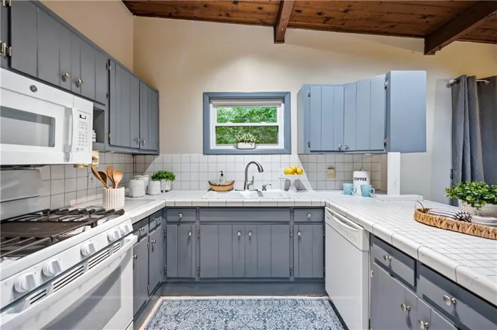 Kitchen featuring exposed wood beam ceilings, white tile countertops, white subway tile backsplash, and blue-gray cabinetry
