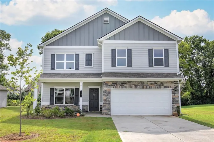 Two-story residence featuring light gray siding with dark gray shutters, a stone accent facade, a two-car garage, and a covered front entry