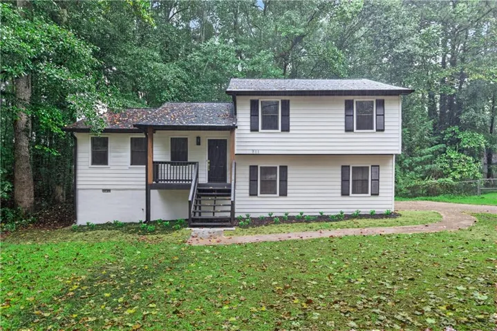 Split-level exterior with white siding and dark shutters, featuring a covered porch with dark railings and natural wood posts, surrounded by mature trees