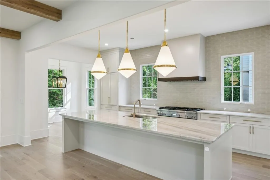 Kitchen featuring pendant lighting, sink, white cabinets, light stone counters, and custom range hood