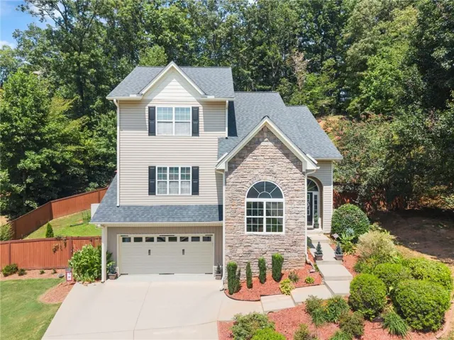 Two-story residence featuring a stone and siding exterior, an arched window, a two-car garage, and a concrete driveway