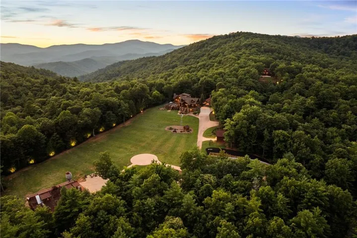Expansive property with a large, manicured lawn, multiple structures, and a winding driveway, all surrounded by dense, mature trees and distant mountains