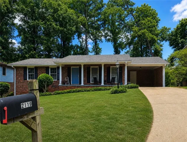 Brick ranch-style residence featuring a covered front porch with white columns, a vibrant blue front door, and a two-car carport