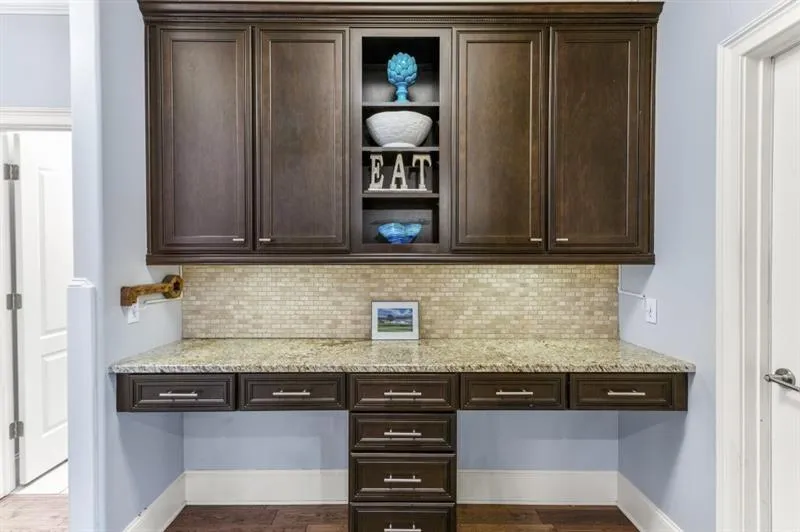 Bar with light stone counters, built in desk, and dark brown cabinets