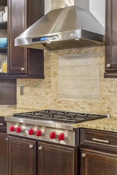 Kitchen with backsplash, ventilation hood, light stone countertops, and stainless steel gas cooktop
