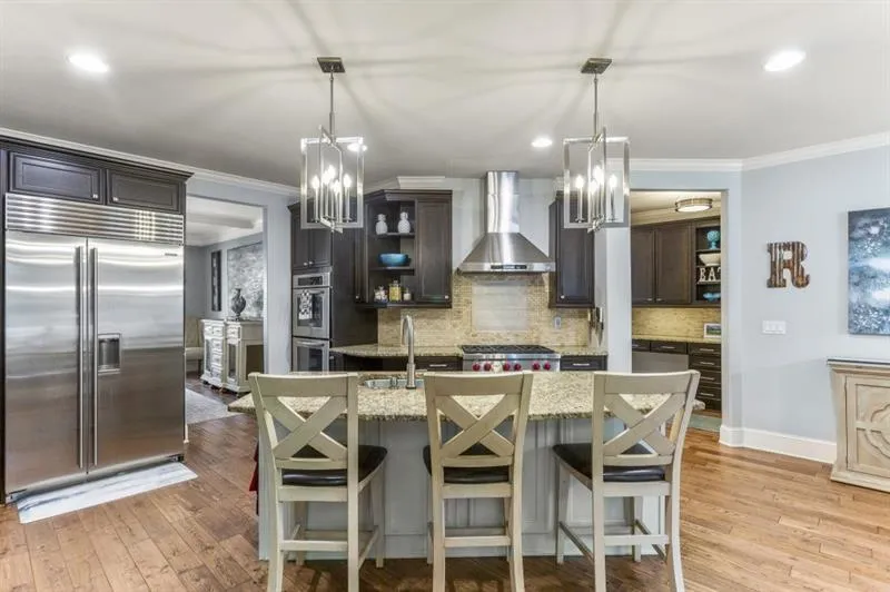 Kitchen with wall chimney range hood, sink, appliances with stainless steel finishes, a kitchen breakfast bar, and light stone counters