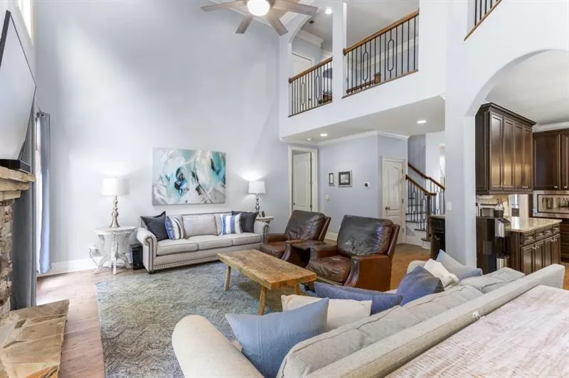 Living room with a stone fireplace, crown molding, wood-type flooring, ceiling fan, and a high ceiling