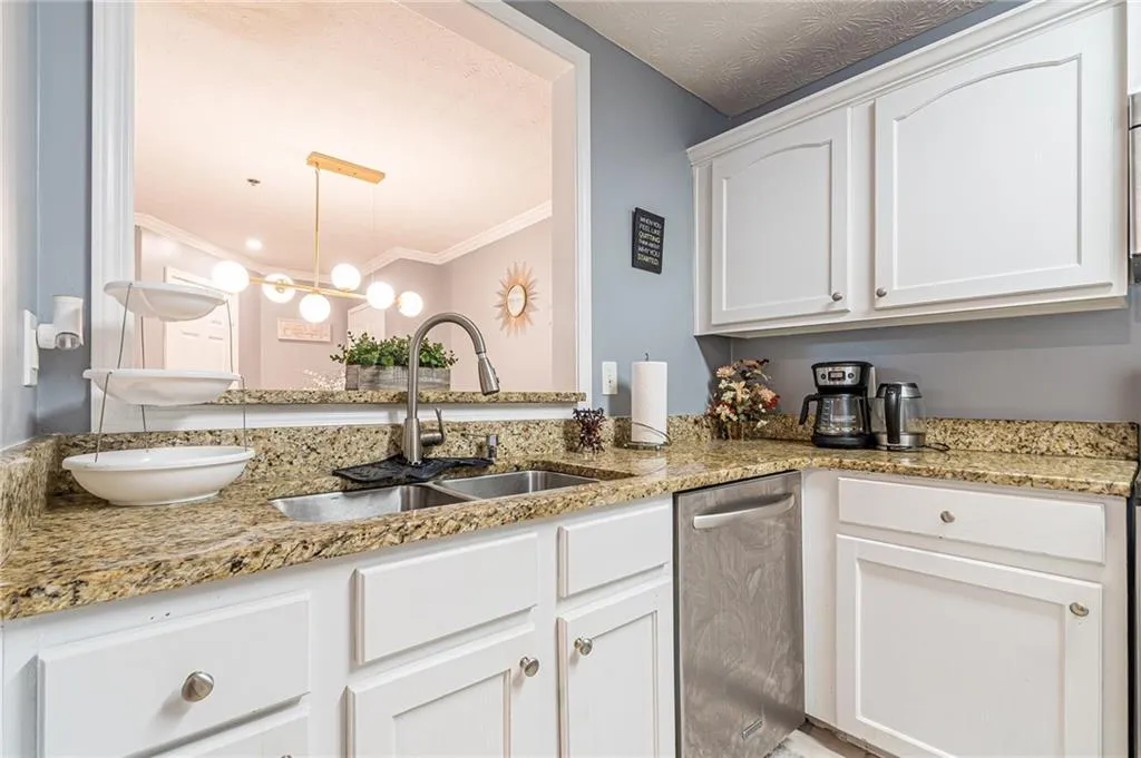 Kitchen with dishwasher, white cabinets, light stone counters, crown molding, and decorative light fixtures