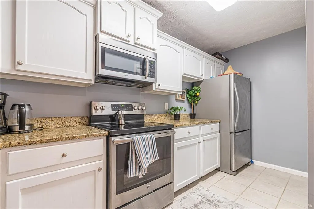 Kitchen with appliances with stainless steel finishes, white cabinets, light tile patterned floors, a textured ceiling, and light stone counters