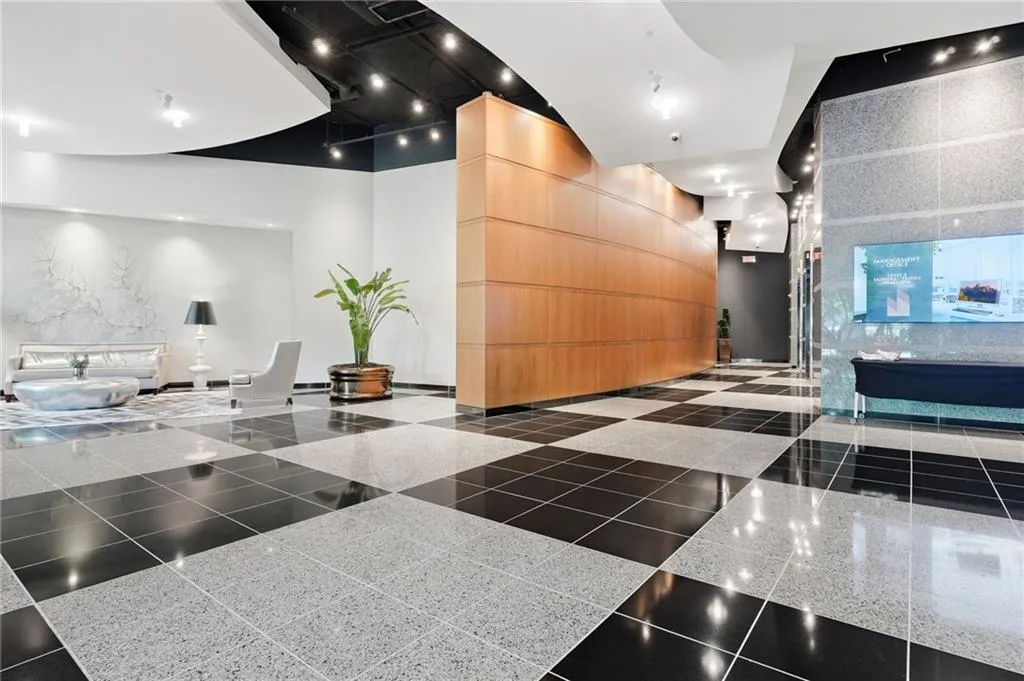 Black and white checkerboard flooring, wood-paneled wall, recessed ceiling lighting, textured wall paneling, and a mounted display screen