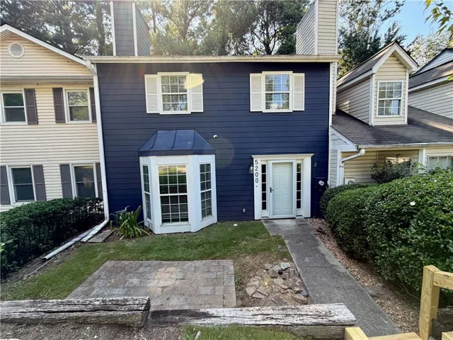 Blue siding exterior with white trim, a bay window with a dark metal roof accent, a white front entry door, and a paved walkway