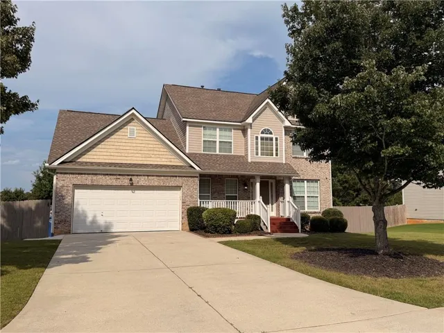 Two-story residence featuring brick and siding facade, covered front porch with white railings, a two-car garage, and a paved driveway