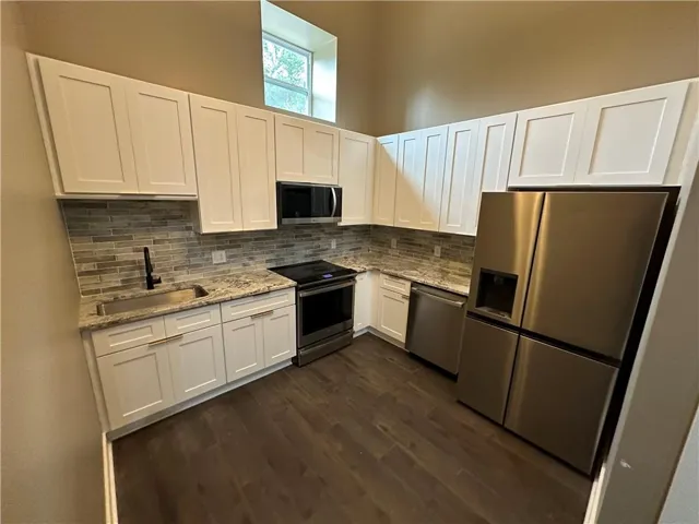 Kitchen featuring stainless steel appliances, white cabinets, light stone counters, and dark wood-type flooring