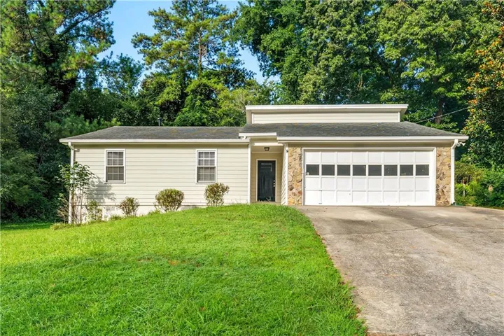 Charming single-story home featuring a brick and vinyl siding exterior, two-car garage with white paneled doors, and a manicured front lawn bordered by mature landscaping