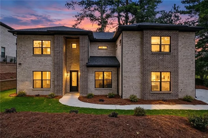 Modern brick exterior with contrasting light and dark brickwork, multiple large windows, and a paved walkway leading to the front entry