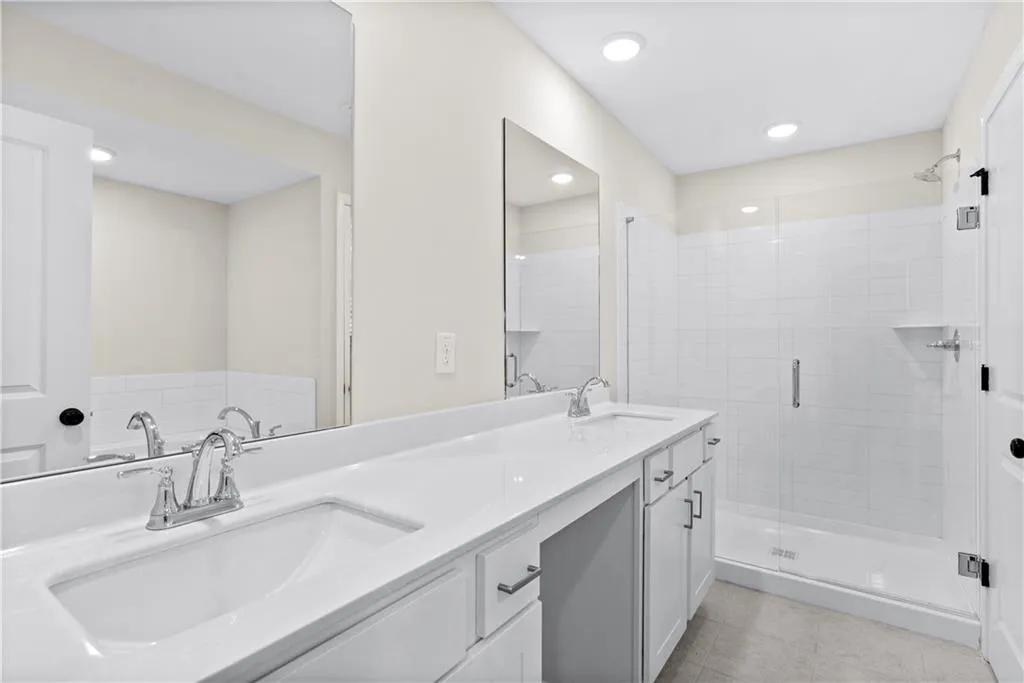 Bathroom with double vanity, a shower stall, light tile patterned floors, and recessed lighting