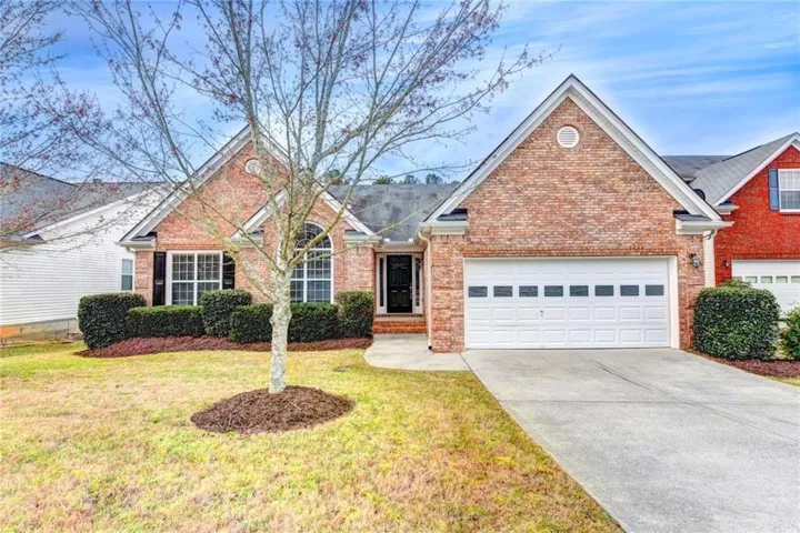Brick exterior with an arched window, two-car garage, concrete driveway, and established front landscaping
