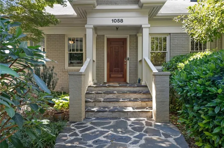 Stone walkway leading to matching stone steps, front porch with white columns, rich wood-panel door, and brick exterior