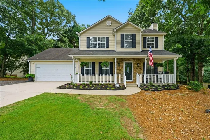 Two-story residence featuring a covered front porch with white railing, stone accents, and a light-toned siding exterior