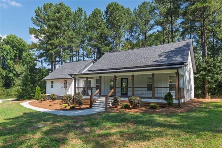 Contemporary farmhouse exterior with white vertical siding, a covered front porch, dark wood columns and railings, and a dark shingled roof