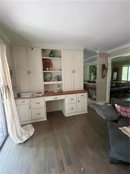 Unfurnished office featuring built in study area, crown molding, and dark wood-style floors